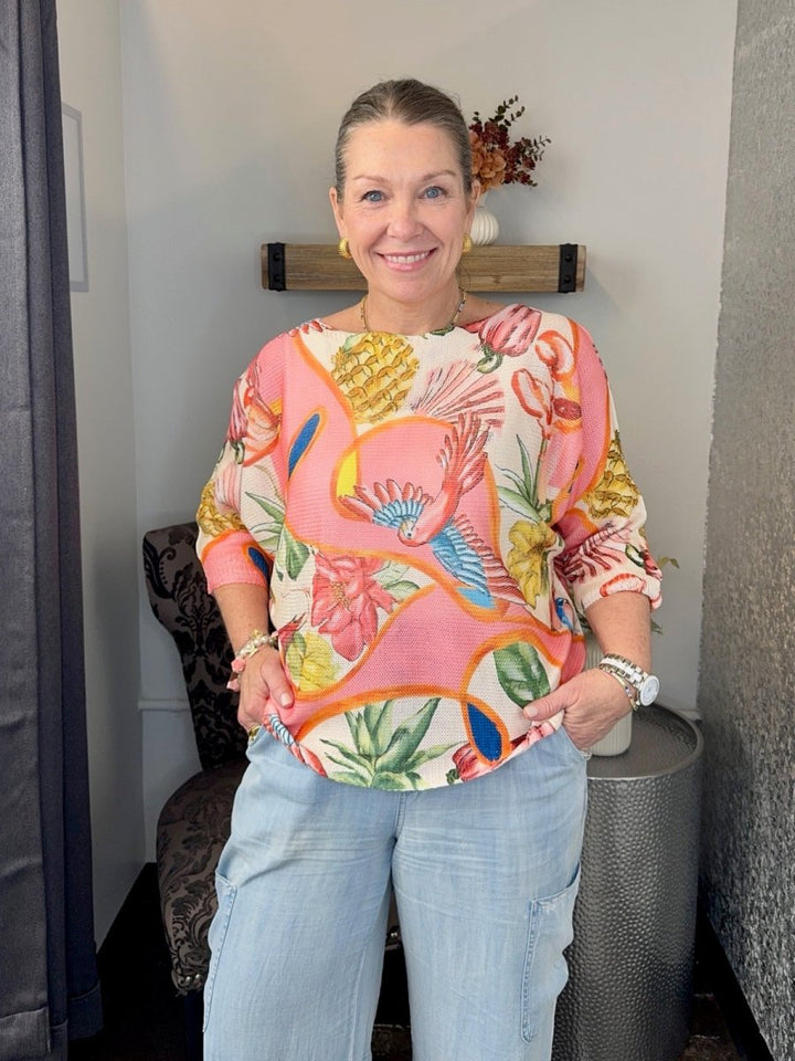Smiling woman wearing a Coral Multi tropical print batwing sweater with 3/4 sleeves and light wash denim jeans.