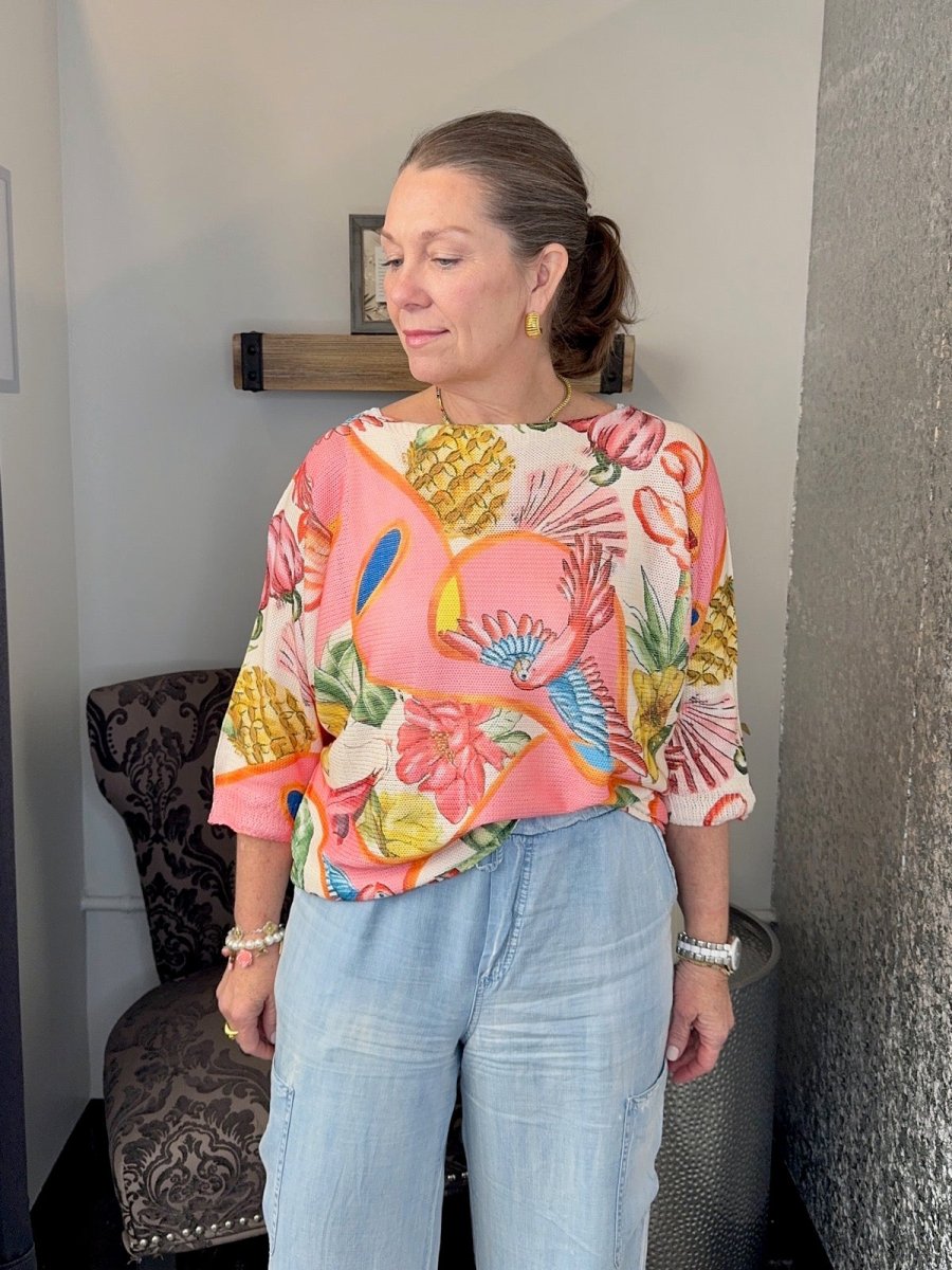 Woman wearing a Coral Multi tropical print batwing sweater with 3/4 sleeves and light wash denim jeans.