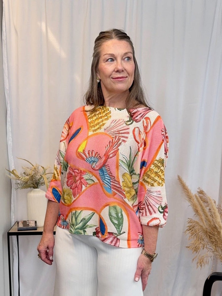 Full length view of the Coral Multi tropical bird print sweater paired with white trousers for a bright, modern aesthetic.