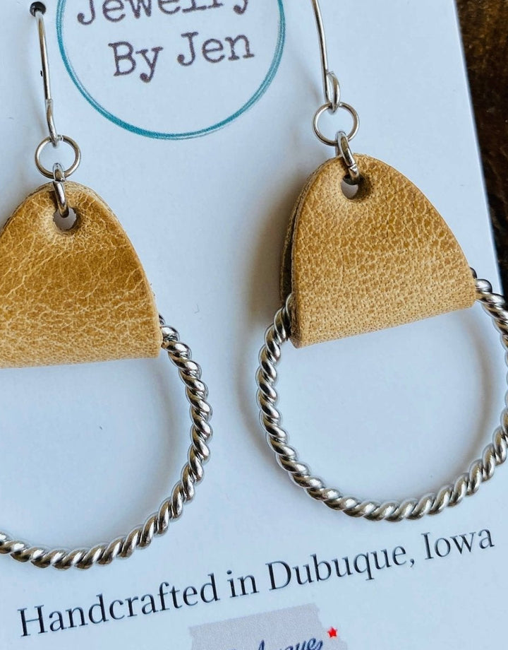 Close up view of an earring with a twisted silver hoop and tan leather.
