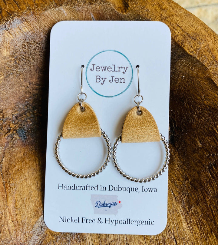 Twisted hoop earrings with weathered tan leather on a stainless steel hoop, displayed on a card with &