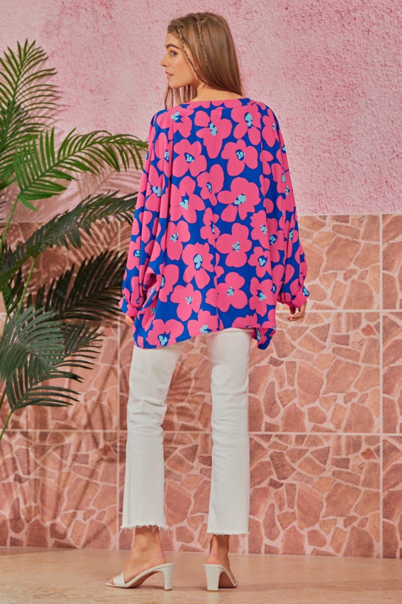 The back view of a lightweight, flowy tunic with a slight high-low hem and a vibrant pink floral pattern on a textured background.