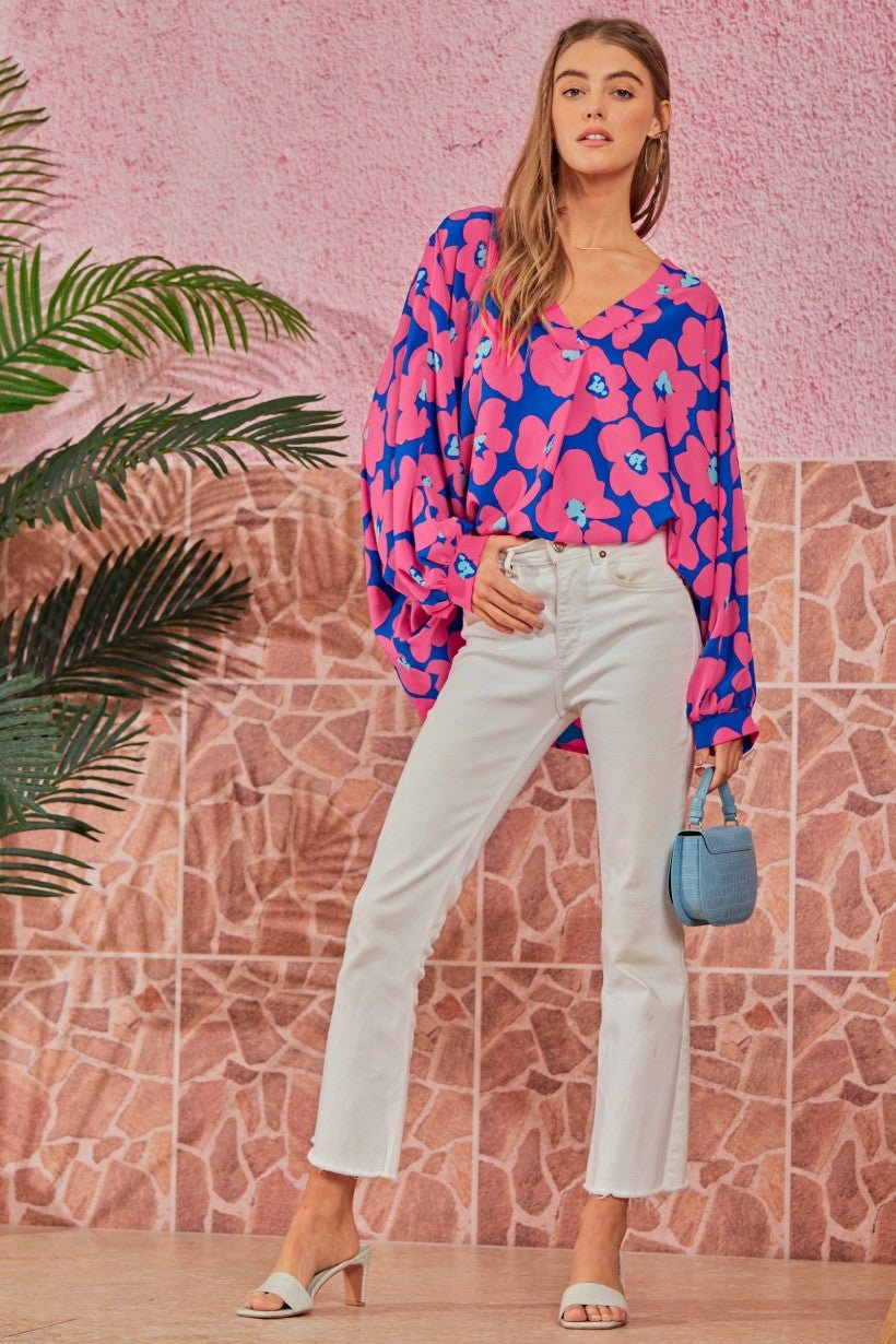 A full-length shot of a model wearing a Floral V-Neck Dolman Top tucked into white flare jeans, paired with white heels and a small blue handbag.